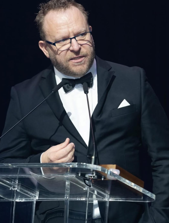 Russell McMullan speaking at a podium
